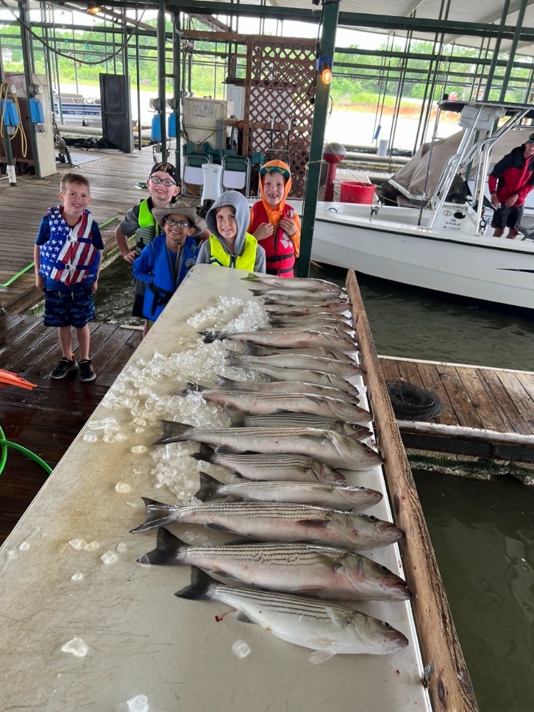 Children in life jackets standing behind a day’s catch at the marina